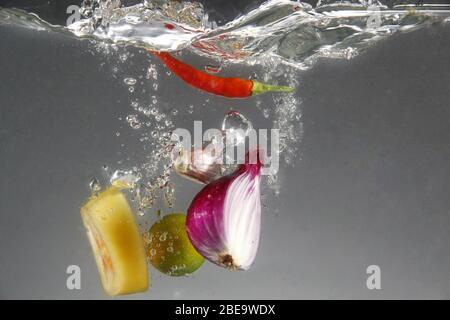 Foto von roten Zwiebeln, roten Chili, Knoblauch, Tomaten und Calamansi in Wasser fallen gelassen Stockfoto