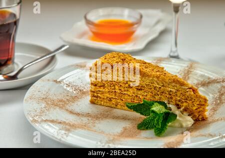 Stück Honigkuchen und frische Minze auf weißem Teller. Serviert mit einer Rosette Honig, einer Tasse aromatischen Tee und einem Glas Weißwein. Stockfoto