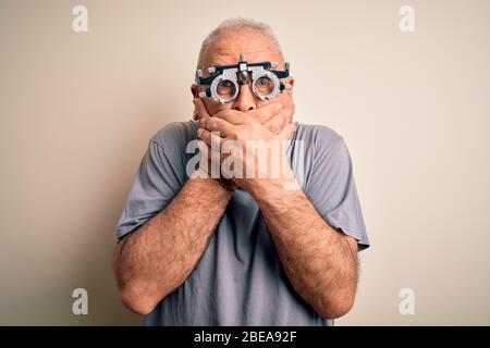 Mittelalter Hoary Mann Kontrolle Vision Tragen Optometrie Brille über weißem Hintergrund schockiert Abdeckung Mund mit Händen für Fehler. Geheimkonzept. Stockfoto