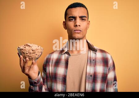 Junge gut aussehende afroamerikanischen Mann hält Schüssel mit gesunden Cornflakes Getreide mit einem selbstbewussten Ausdruck auf intelligente Gesicht denken ernst Stockfoto