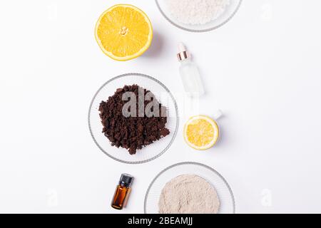 Zutaten für selbstgemahlenes Körperpeeling aus gemahlenem Kaffee, Meersalz, Ton und ätherischem Orangenöl, flach auf weißem Tisch gelegt. Stockfoto