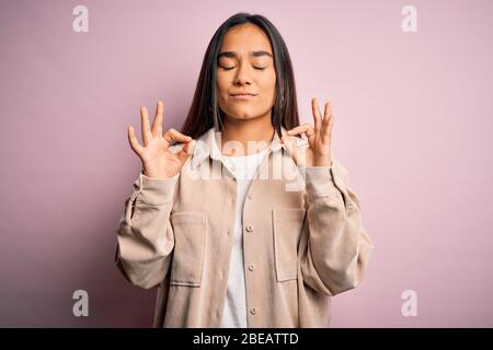 Junge schöne asiatische Frau mit lässigen Hemd über rosa Hintergrund entspannt und lächelnd mit geschlossenen Augen tun Meditation Geste mit fing stehen Stockfoto