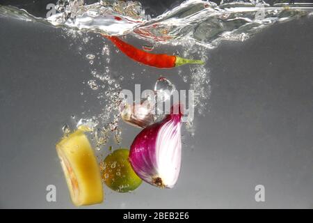 Foto von roten Zwiebeln, roten Chili, Knoblauch, Tomaten und Calamansi in Wasser fallen gelassen Stockfoto