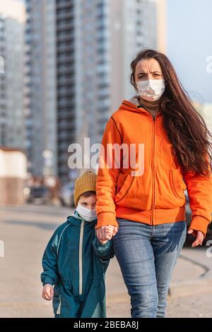 Eine Frau mit einem Kind in medizinischen Masken geht die Straße entlang während der Coronavirus-Pandemie und Covid -19. Stockfoto