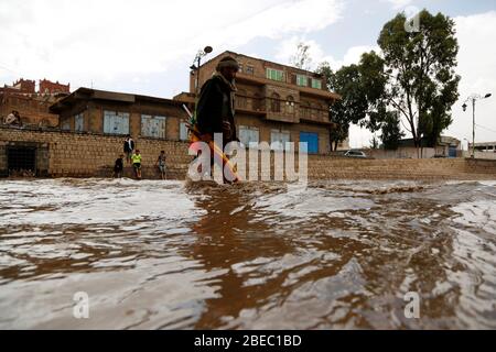 Sanaa, Jemen. April 2020. Ein Mann überquert eine überflutete Straße nach starkem Regen in Sanaa, Jemen, 13. April 2020. Am Montag traf Sanaa ein heftiger Regen. Kredit: Mohammed Mohammed/Xinhua/Alamy Live News Stockfoto