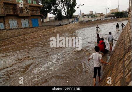 Sanaa, Jemen. April 2020. Kinder versuchen, nach starkem Regen in Sanaa, Jemen, am 13. April 2020, eine überflutete Straße zu überqueren. Am Montag traf Sanaa ein heftiger Regen. Kredit: Mohammed Mohammed/Xinhua/Alamy Live News Stockfoto