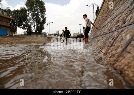 Sanaa, Jemen. April 2020. Kinder versuchen, nach starkem Regen in Sanaa, Jemen, am 13. April 2020, eine überflutete Straße zu überqueren. Am Montag traf Sanaa ein heftiger Regen. Kredit: Mohammed Mohammed/Xinhua/Alamy Live News Stockfoto