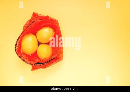 Frische Zitronen in einem roten Beutel zum Verpacken von Gemüse und Obst auf gelbem Hintergrund. Selektiver Fokus. Stockfoto