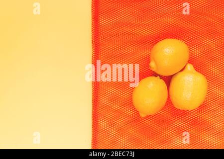 Frische Zitronen in einem roten Beutel zum Verpacken von Gemüse und Obst auf gelbem Hintergrund. Selektiver Fokus. Stockfoto