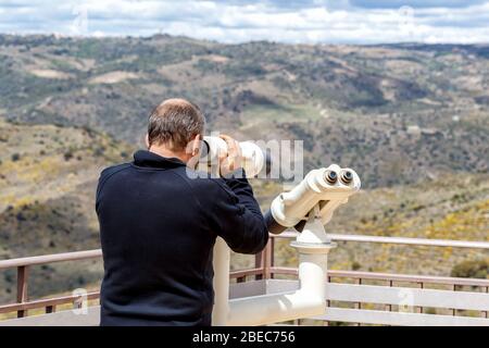 Mann, der durch ein Fernglas mit hoher Leistung auf einen malerischen Bergaussicht blickt. Sierras de Francia und von Béjar. UNESCO-Weltkulturerbe in Spanien. Stockfoto