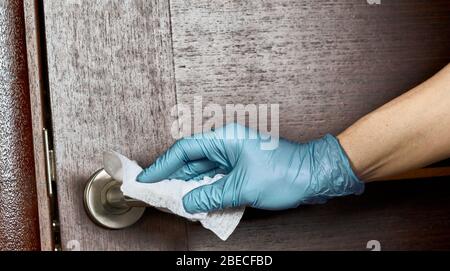 Reinigen, desinfizieren, den Türgriff aus Chrom mit einer Hand im Handschuh und Serviette ganz nah abwischen. Stockfoto