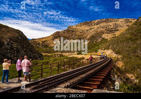 Touristen beobachten die Pukerangi Zug von DJ3211 überqueren Sie die Tiefe Stream Viadukt über die Dunedin Eisenbahn, ehemalige Taieri Gorge Railway geschleppt. Otago, Stockfoto