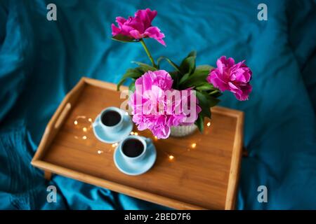 Schöne rosa Pfingstrosen und zwei Tassen Kaffee stehen auf einem Holz- Fach im Bett. Close-up. Ansicht von oben Stockfoto