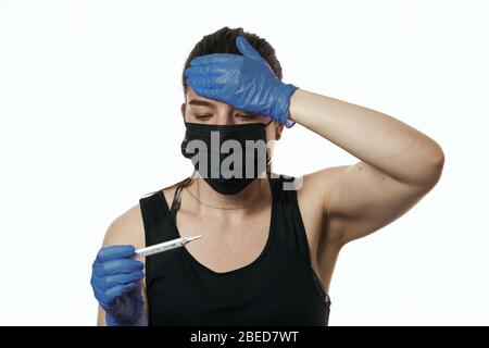 Das Mädchen in der medizinischen Maske schaut auf das Thermometer und runzelt die Stirn. Hohe Temperatur bei einem Kranken. Konzept der Virusepidemie. Nahaufnahme Stockfoto