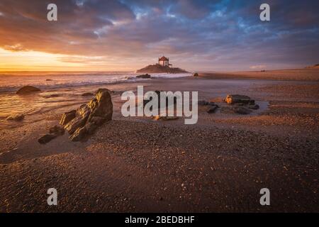 Schöne Kirche am Strand. Capela Senhor da Pedra, bei Sonnenuntergang, mit Wellen über der Kirche Stockfoto