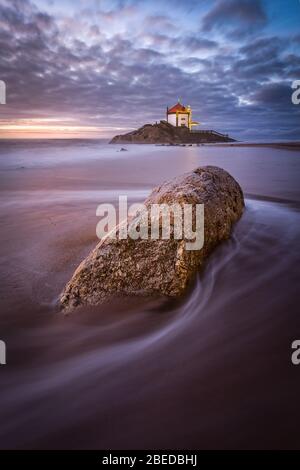 Schöne Kirche am Strand. Capela Senhor da Pedra, bei Sonnenuntergang, mit Wellen über der Kirche Stockfoto