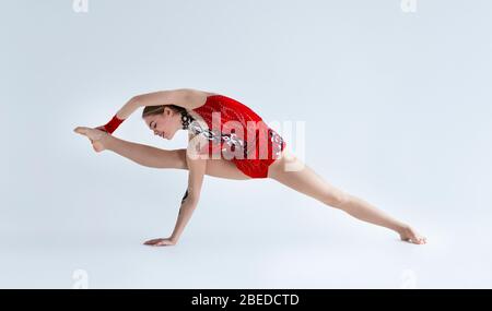 Junge Turnerin Mädchen Stretching und Training in roten Sportanzug, weißem Hintergrund Stockfoto