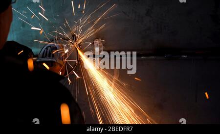 Ein Arbeiter, der ein Mahlwerk verwendet, zerschnitt Metall. Verarbeitung eines Metallprodukts mit einem manuellen Mahlwerk. Stockfoto