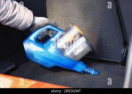 Staubsauger in den Händen des Fahrers. Reinigung des Kofferraums des Autos mit blauem Staubsauger. Das Auto wird regelmäßig gereinigt. Stockfoto