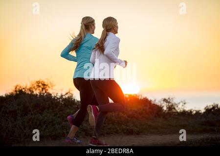 Zwei junge Frauen joggen bei Sonnenuntergang gemeinsam entlang der Klippen am Meer Stockfoto