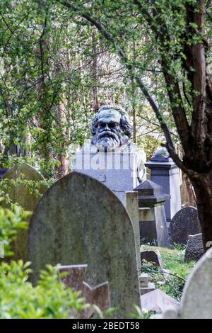 Die Büste von Karl Marx blickt durch die Grabsteine und das Laub seines Denkmals auf dem Highgate Cemetery, North London, Großbritannien Stockfoto