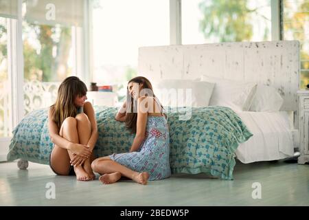 Zwei lächelnde junge Frauen sitzen auf dem Schlafzimmerboden und unterhalten sich miteinander Stockfoto