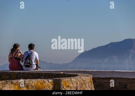 Tarifa, Spanien. Februar 2020. Ein Paar sitzt auf einem Aussichtspunkt in Andalusien und blickt auf das Atlasgebirge in Marokko über die Meerenge von Gibraltar Stockfoto