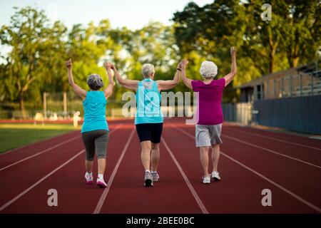 Ältere Frauen halten sich die Hände, während sie auf einer athletischen Strecke laufen Stockfoto