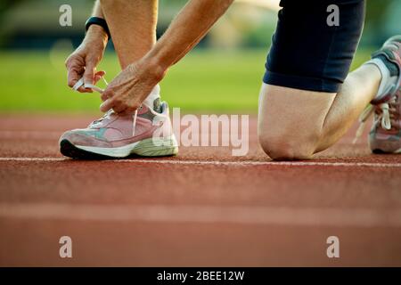 Ältere Frau, die ihr Schuhstück auf einer Laufstrecke festbänd Stockfoto