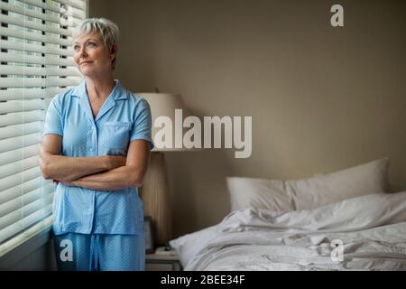 Reife Frau schaut durch ein Fenster, nachdem sie aus dem Bett Stockfoto