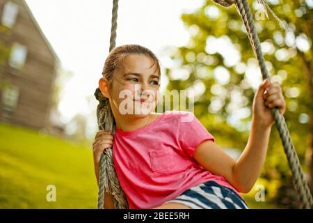 Porträt eines glücklichen jungen Mädchens, das auf einer Seilschaukel spielt Stockfoto