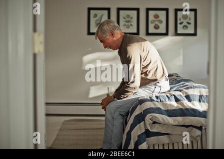 Porträt eines besorgten älteren Mannes, der allein auf einem Bett sitzt Stockfoto