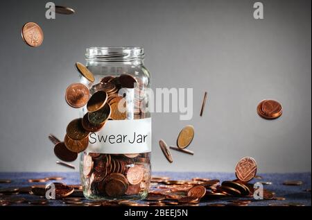 Münzen fallen auf ein Schimpfglas voller britischer Sterling Stockfoto