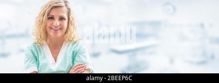 Blonde Ärztin lächelt in die Kamera, Arme auf der Brust gekreuzt, in hellgrüner Uniform mit verschwommenem Laborhintergrund gekleidet, in einem Verbot Stockfoto