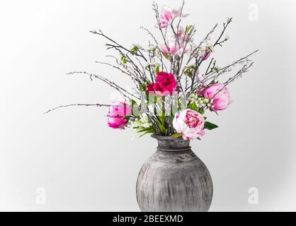 Wilder moderner Frühlingsstrauß mit rosa Pfingstrosen, Magnolienzweigen, Maiglöckchen und Weidenkatzen auf weißem Hintergrund. Nahaufnahme. Stockfoto