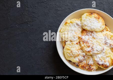 Süße Quark-Pfannkuchen auf dunklem Hintergrund. Pfannkuchen mit Quark auf einem weißen Teller mit Puderzucker bestreut. Kopierbereich. Stockfoto