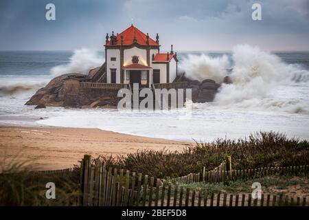 Schöne Kirche am Strand. Capela Senhor da Pedra, bei Sonnenuntergang, mit Wellen über der Kirche Stockfoto