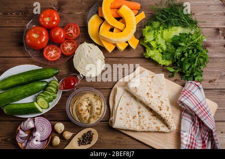 Zubereitung von Zutaten für die Zubereitung von hausgemachter vegetarischer Shawarma mit Hummus und Gemüse auf dunklem Holzhintergrund mit Zutat Stockfoto