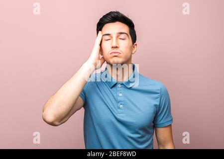 Coronavirus Pandemie nur schlechte Nachrichten. Erschöpfter Erwachsener Mann in blauem Hemd mit Kopfschmerzen, die Hand über seinem Tempel vor rosa Hintergrund stehend Stockfoto