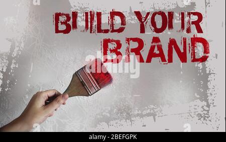 Bauen Sie Ihre Markenworte auf graue Wand mit Pinsel in der Hand. Motivierendes Geschäftsmarketing-Konzept Stockfoto