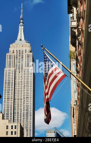 Das berühmte Empire State Building wird mit einer amerikanischen Flagge auf der Fifth Avenue, New York City, USA, besichtigt Stockfoto