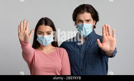 Soziale Distanz. Ernstes Millennial-Paar in medizinischen Masken zeigt Stop-Geste Stockfoto