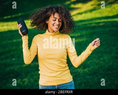 Moderne trendy afroamerikanischen Mädchen hören Musik von drahtlosen tragbaren speaker.Young schöne Frau genießen, tanzen im Park. Stockfoto