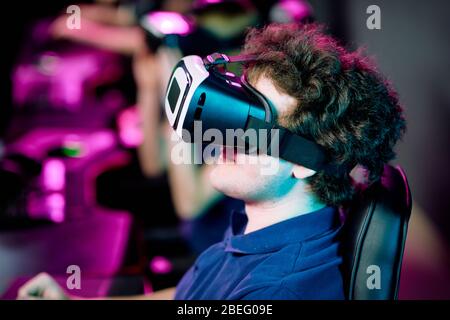 Seitenansicht des positiven jungen lockigen Gamer, der Videospiel in Virtual Reality Brille spielt Stockfoto