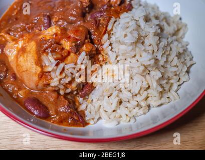 Von oben nach unten und aus der Nähe sehen Sie süßes und würziges südamerikanisches Hühnermole und gesundes braunes Vollkornreis-Abendessen in einer roten Servierschüssel Stockfoto