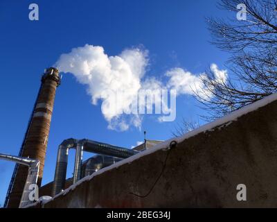 Rohre einer alten Fabrik werfen Wolken von giftigem weißem Rauch in den Himmel, die die Atmosphäre schädigen. Urbaner Smog aus Rauch aus Kesselhäusern. Weißer Rauch aus einem Kamin gegen einen blauen klaren Himmel. Stockfoto