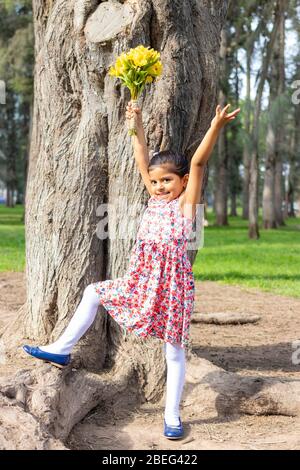 Kleines Mädchen im Kleid feiert im Park mit einem Blumenstrauß in der Hand Stockfoto