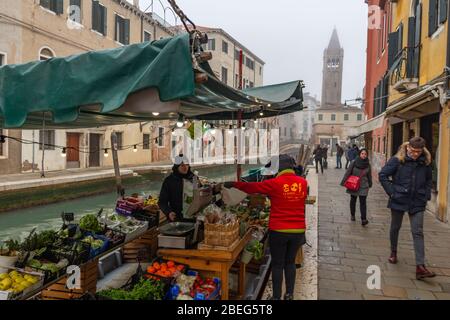 Venedig, Italien. Januar 2019. Leute, die in einem lokalen Lebensmittelgeschäft ein Boot auf einem venezianischen Kanal während eines nebligen Morgens kaufen Stockfoto