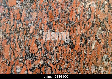 Roter Granit Hintergrund. Die Textur des alten Granits. Rot polierter Granit mit Kratzern und Rissen. Die Textur des Natursteins. Nahaufnahme. Stockfoto