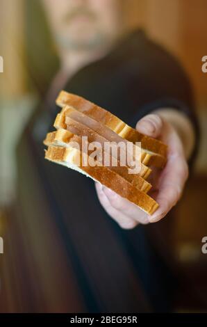 Ein Mann teilt sich Essen. Eine männliche Hand hält Brotscheiben in die Kamera. Hilfe für die Armen und Bedürftigen. Selektiver Fokus. Unscharfer Hintergrund. Stockfoto